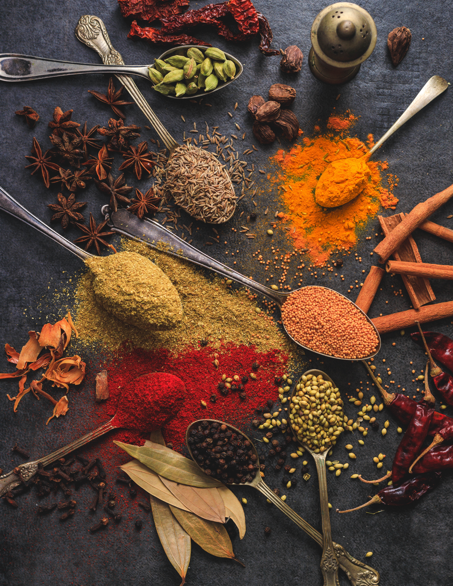 Mélange coloré d'épices du monde comme le curcuma, le cumin, le paprika et la cannelle, sur une table en pierre noire – cuisine internationale et voyage culinaire